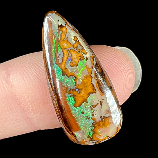 A pear shaped boulder opal stone with bright green color play.