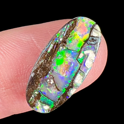 A loose, oval cut boulder opal stone from Koroit, Australia.  The opal shines green and blue colors.