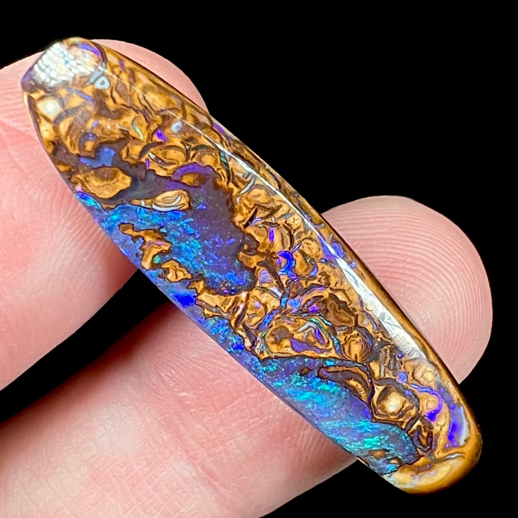 A polished boulder opal stone from Koroit, Australia.  The stone has blue and purple veins.