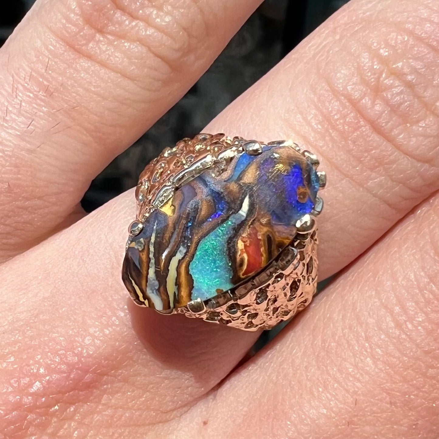 A yellow gold solitaire ring mounted with a Koroit boulder opal stone that shows the picture of a peacock.