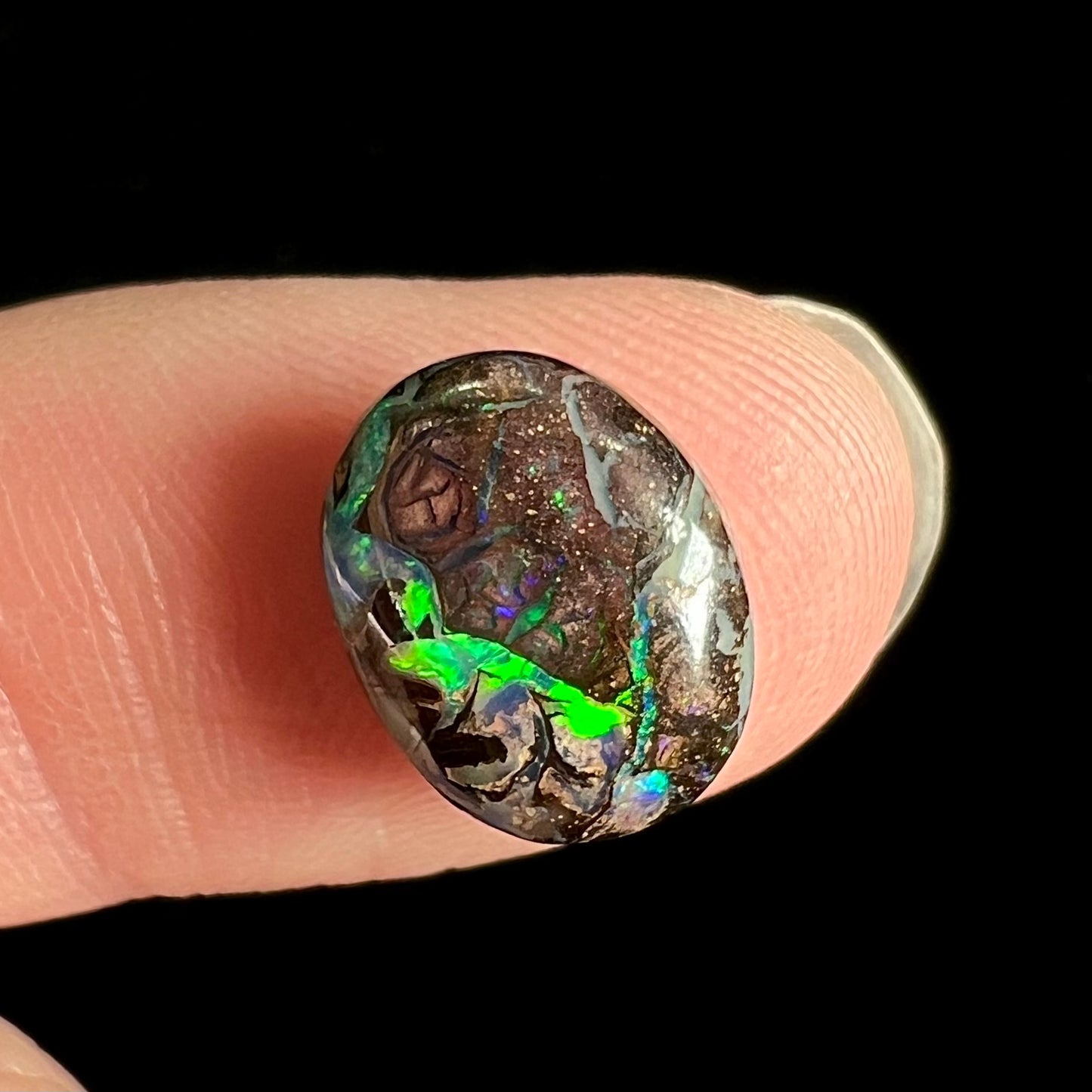 A loose, oval cabochon cut boulder opal stone from Koroit, Australia.  The opal has a bright green flash.