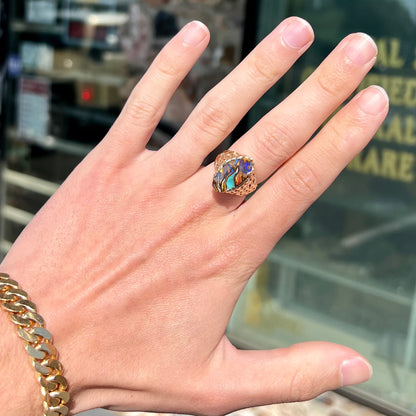 A yellow gold solitaire ring mounted with a Koroit boulder opal stone that shows the picture of a peacock.