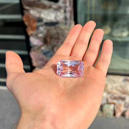 A loose, radiant cut kunzite gemstone.  The stone is a light purplish pink color.