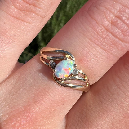 A yellow gold ring mounted with two diamond accents and an oval cut lab created opal.  The opal has bright red colors.