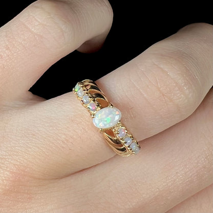 A yellow gold ring featuring two crossing, alternating lines of round cut synthetic opals.  In the middle is a larger oval cut synthetic opal.