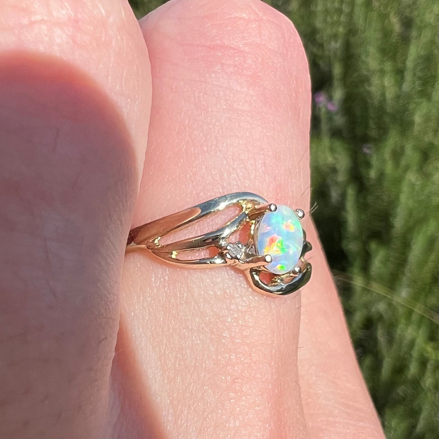 A yellow gold ring mounted with two diamond accents and an oval cut lab created opal.  The opal has bright red colors.