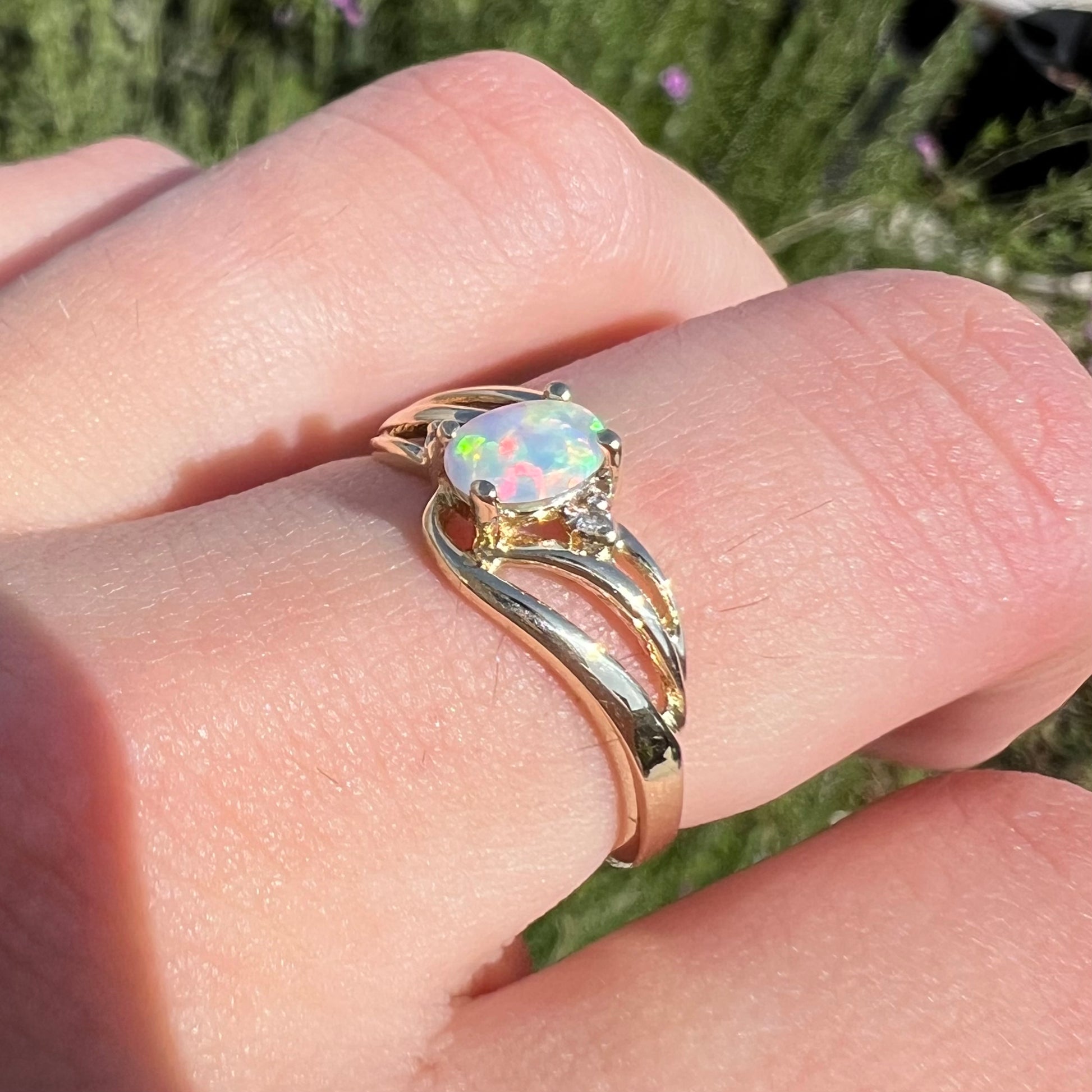 A yellow gold ring mounted with two diamond accents and an oval cut lab created opal.  The opal has bright red colors.