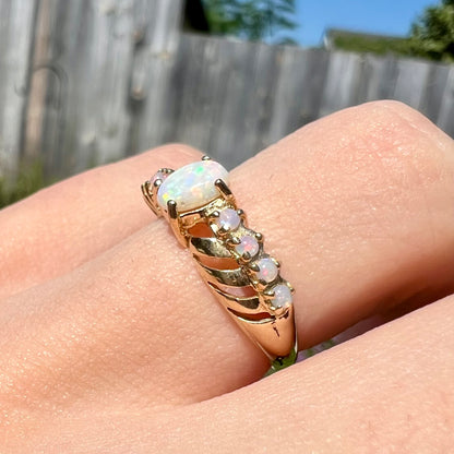 A yellow gold ring featuring two crossing, alternating lines of round cut synthetic opals.  In the middle is a larger oval cut synthetic opal.