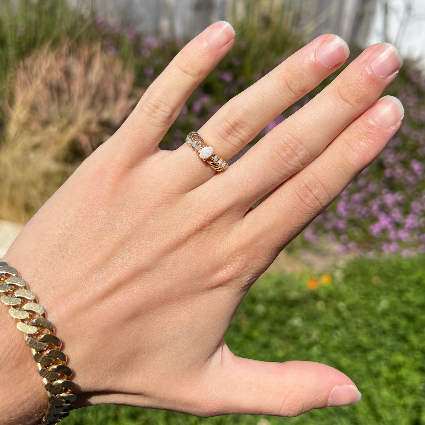 A yellow gold ring featuring two crossing, alternating lines of round cut synthetic opals.  In the middle is a larger oval cut synthetic opal.