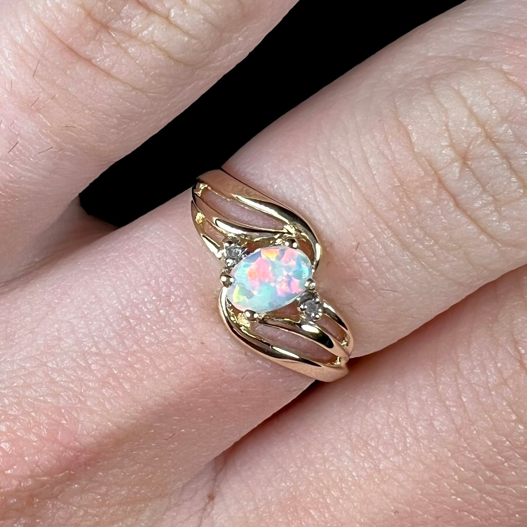 A yellow gold ring mounted with two diamond accents and an oval cut lab created opal.  The opal has bright red colors.