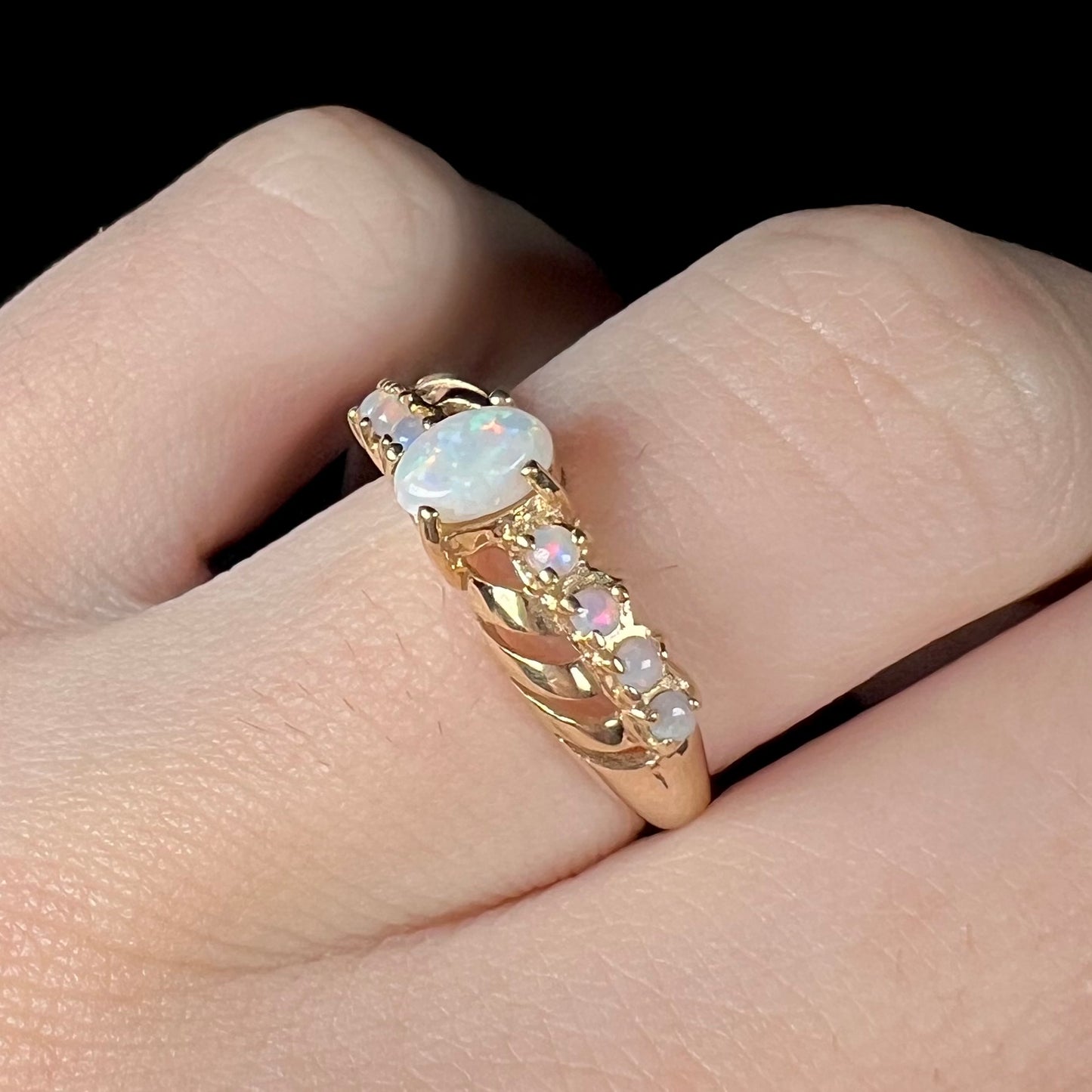 A yellow gold ring featuring two crossing, alternating lines of round cut synthetic opals.  In the middle is a larger oval cut synthetic opal.