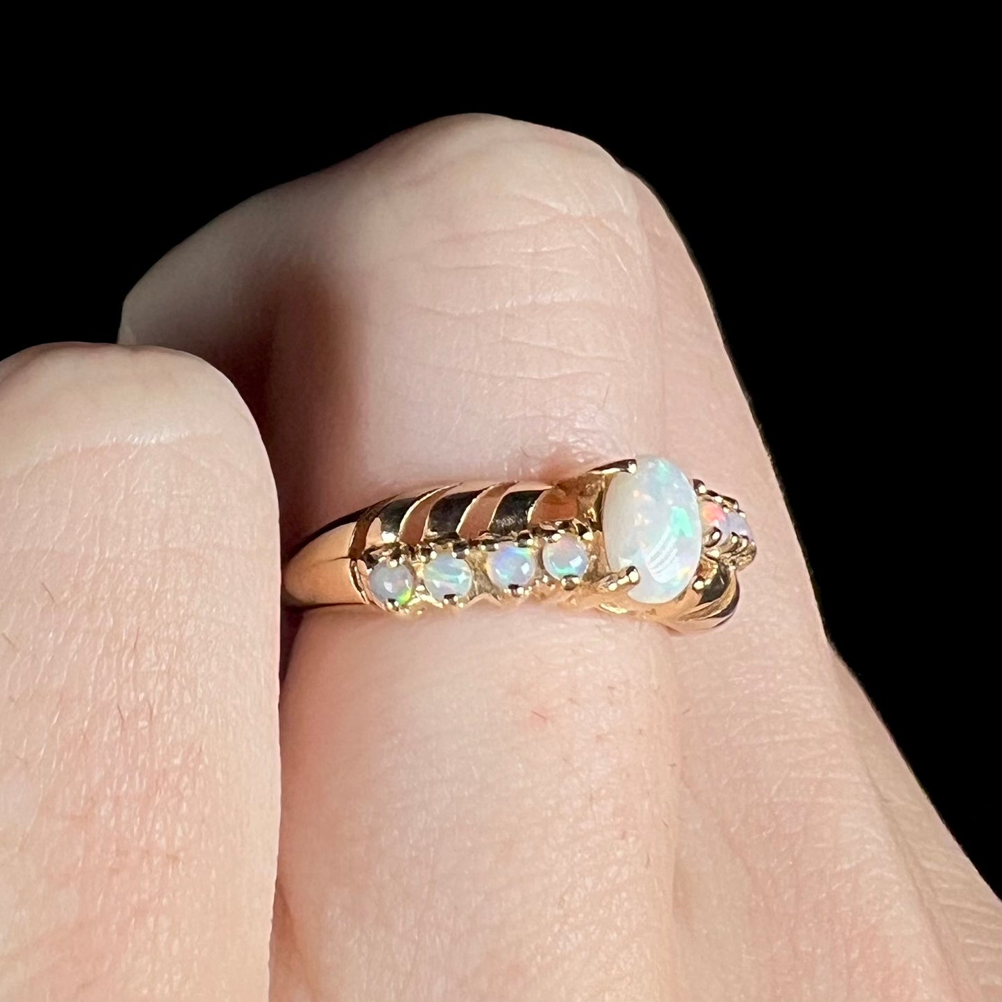 A yellow gold ring featuring two crossing, alternating lines of round cut synthetic opals.  In the middle is a larger oval cut synthetic opal.