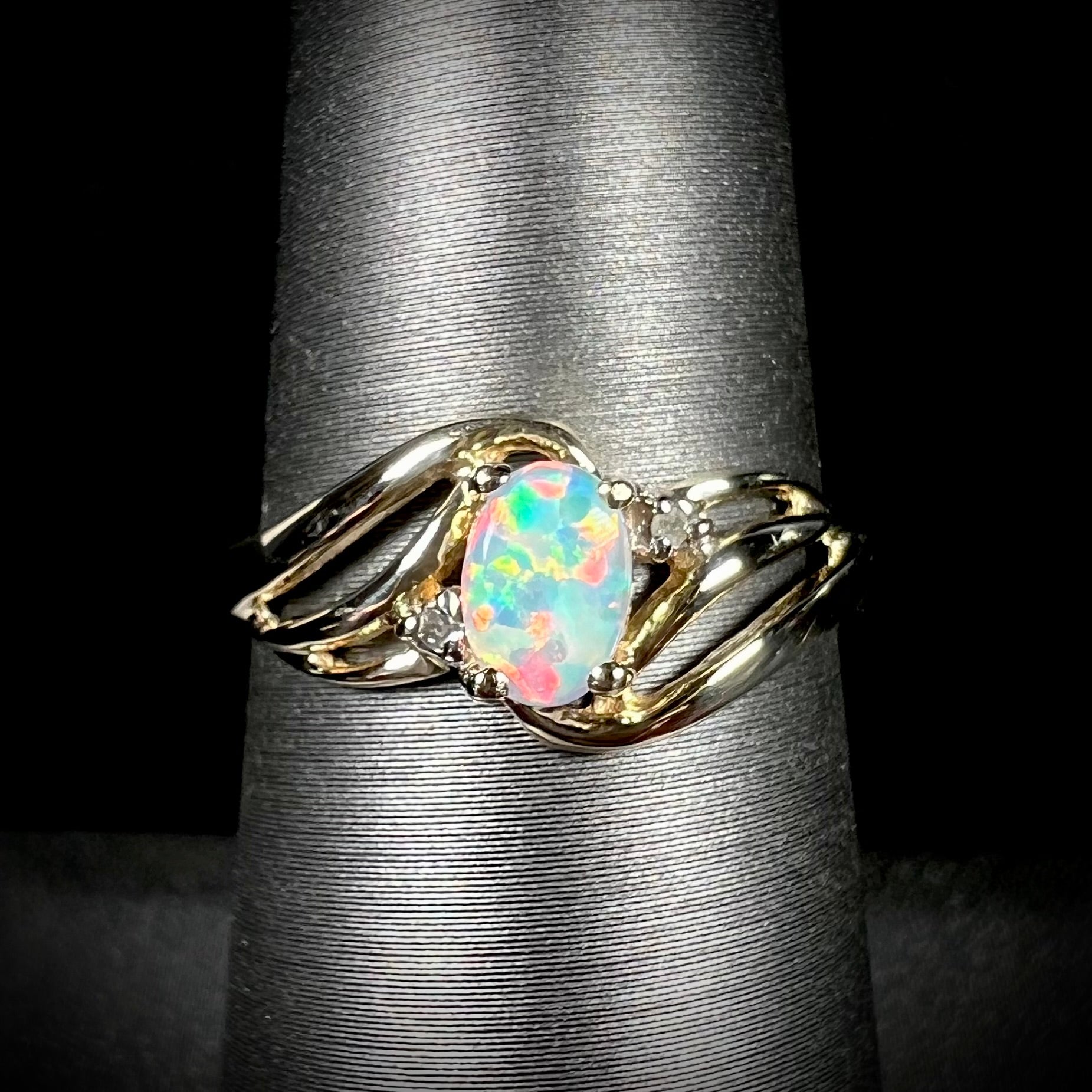 A yellow gold ring mounted with two diamond accents and an oval cut lab created opal.  The opal has bright red colors.