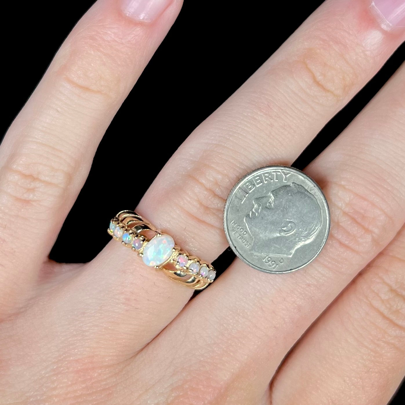 A yellow gold ring featuring two crossing, alternating lines of round cut synthetic opals.  In the middle is a larger oval cut synthetic opal.