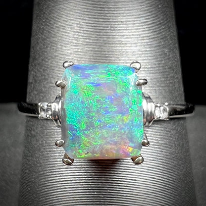 A ladies' white gold ring set with a rectangle cut black opal stone with round white sapphire accent stones.