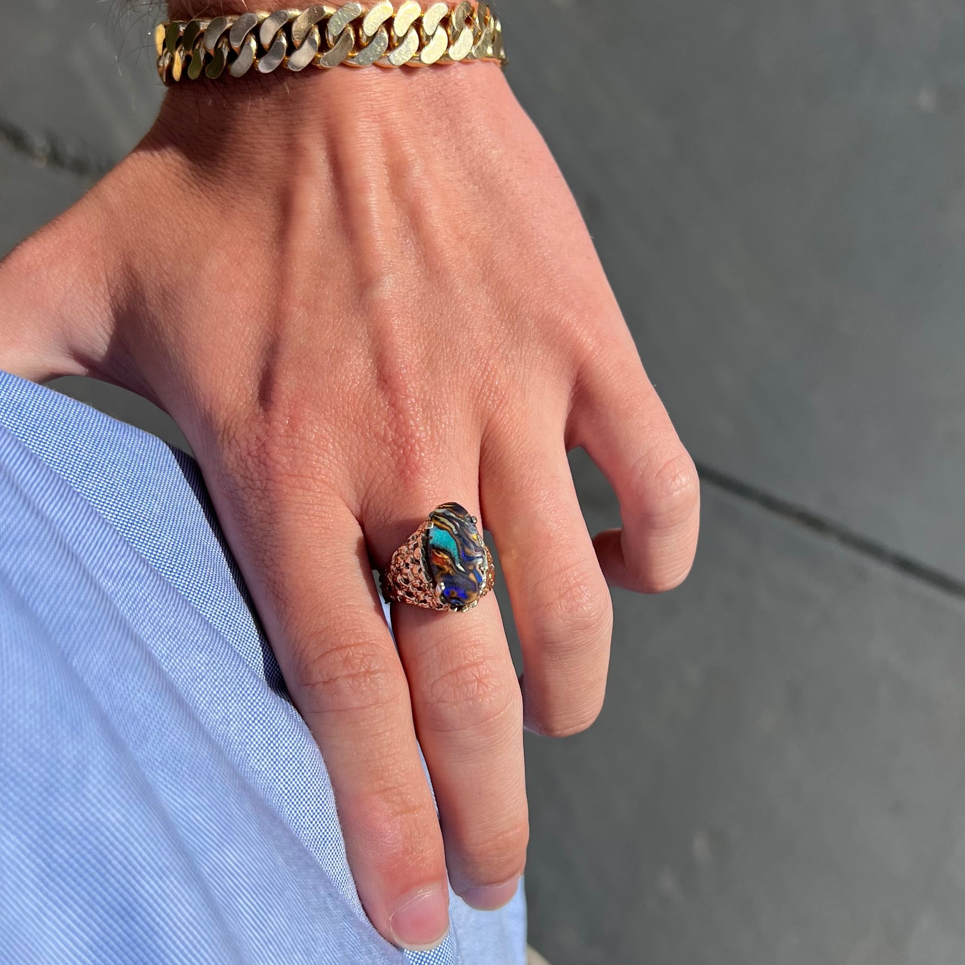 A yellow gold solitaire ring mounted with a Koroit boulder opal stone that shows the picture of a peacock.