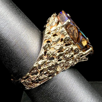 A yellow gold solitaire ring mounted with a Koroit boulder opal stone that shows the picture of a peacock.