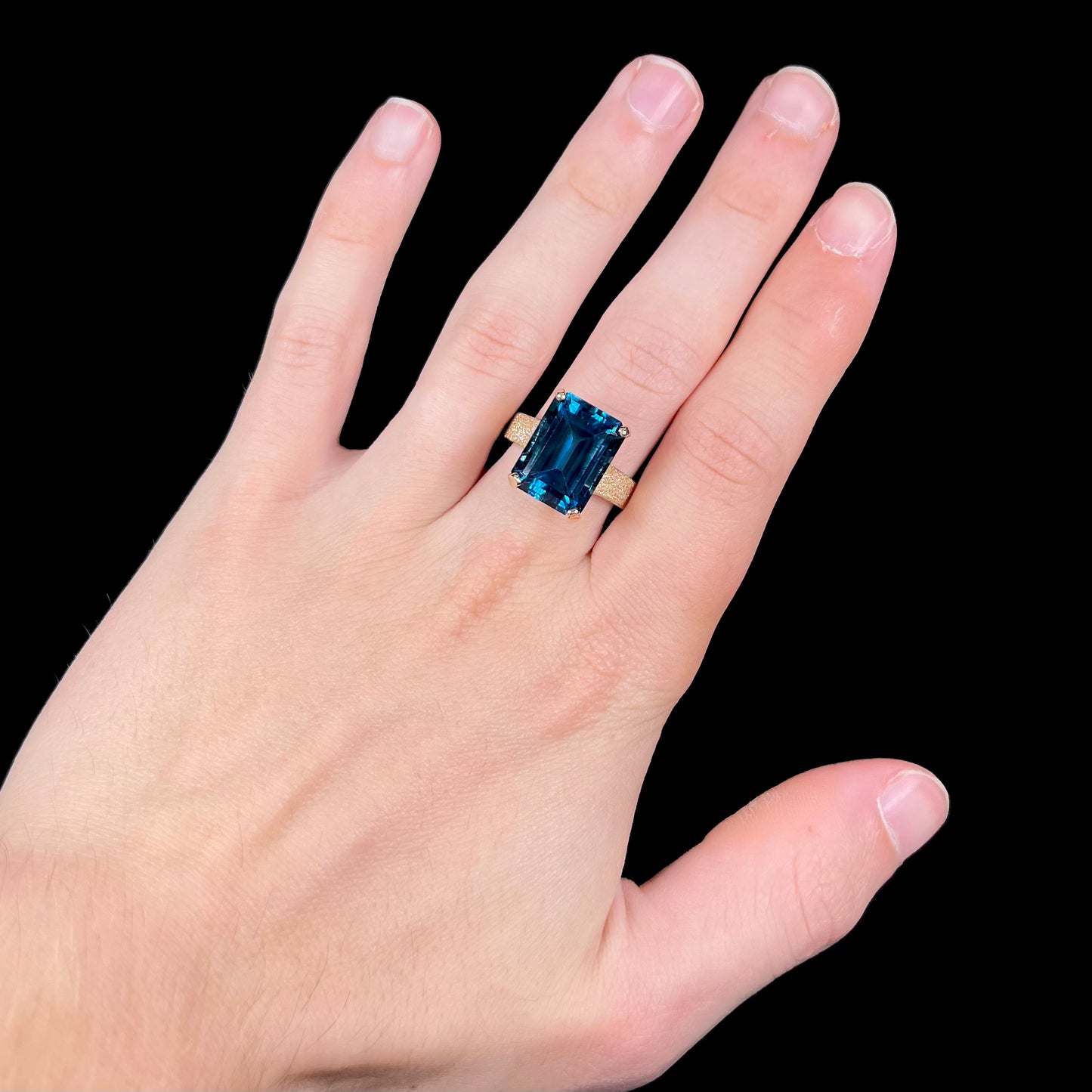 A ladies' yellow gold London blue topaz solitaire ring.  The ring is textured, and the topaz is emerald cut.