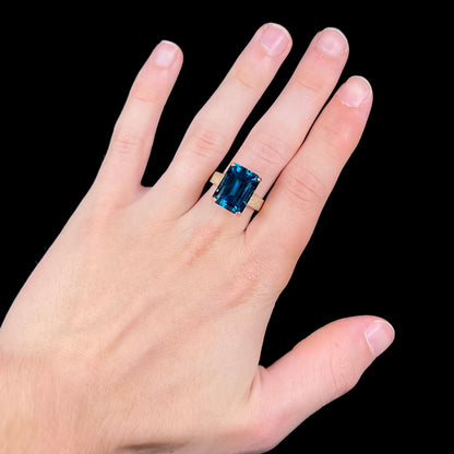 A ladies' yellow gold London blue topaz solitaire ring.  The ring is textured, and the topaz is emerald cut.