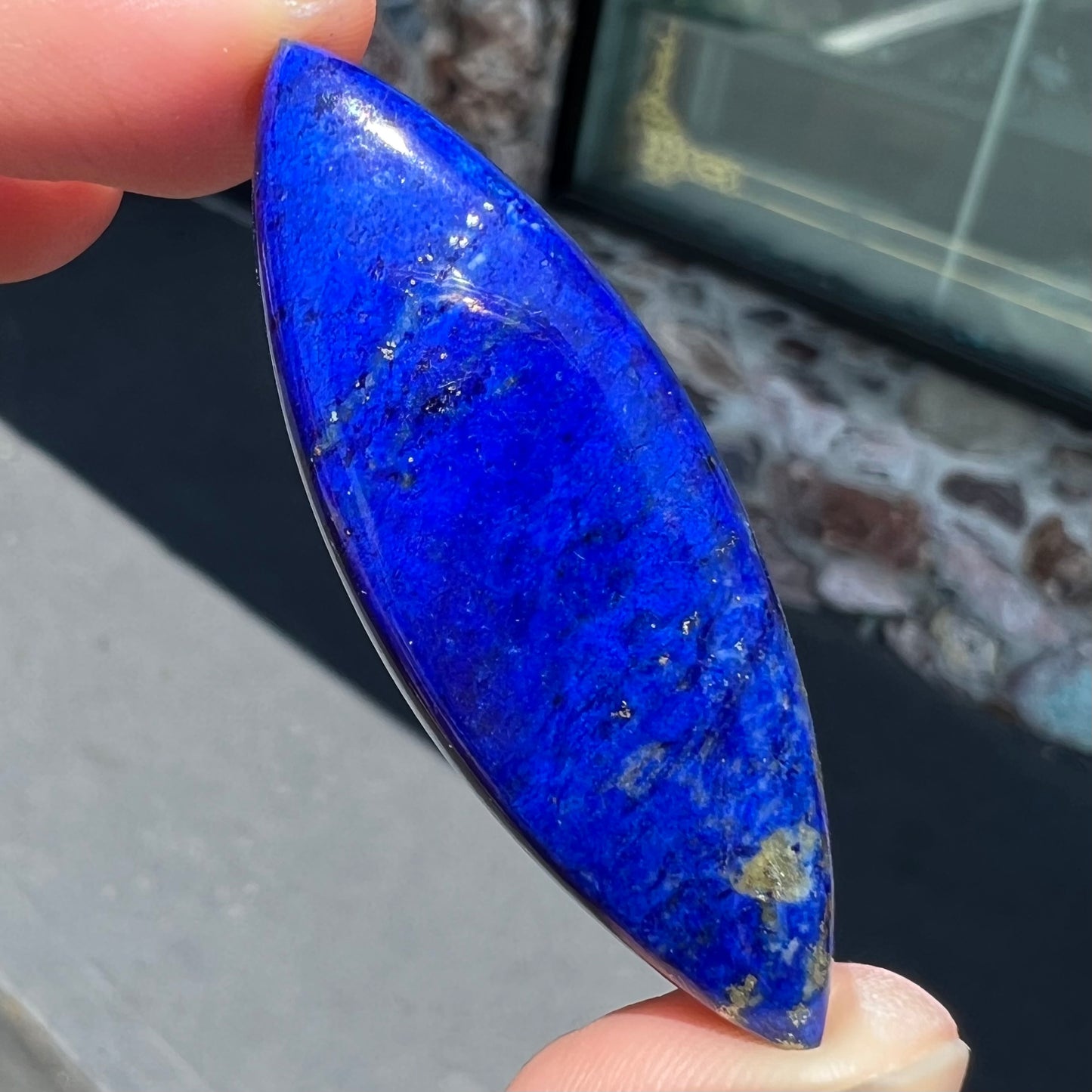 A loose, marquise cabochon cut lapis lazuli stone.  The stone has pyrite inclusions.