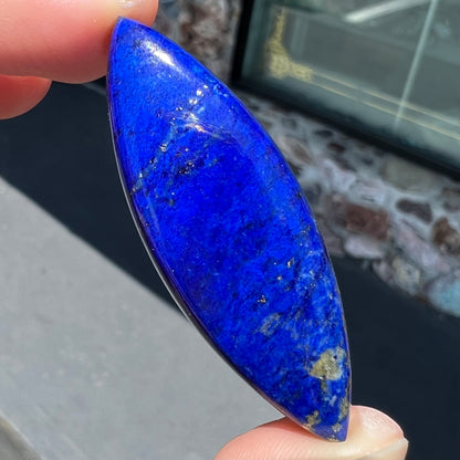 A loose, marquise cabochon cut lapis lazuli stone.  The stone has pyrite inclusions.