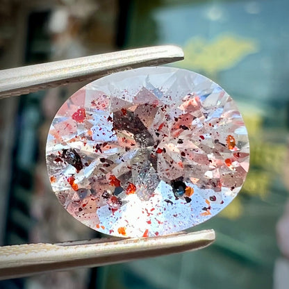 A loose, faceted oval cut lepidocrocite quartz stone.  The stone has red and black inclusions.