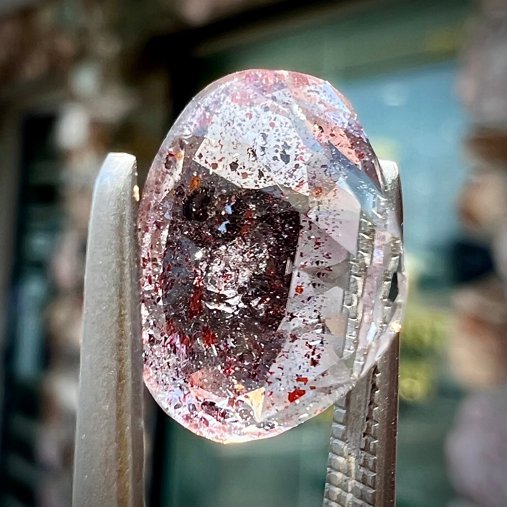 A loose, faceted oval cut lepidocrocite quartz stone.  The stone has red and black inclusions.