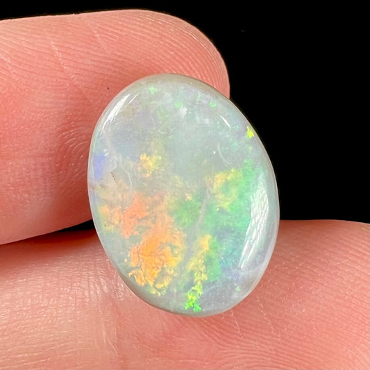 A loose, oval cut light opal stone from Mintabie, Australia.  The stone shows dull orange and green colors.