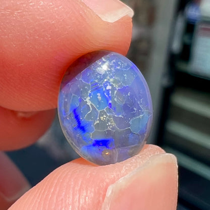 A loose, oval cabochon cut black crystal opal from Lightning Ridge, Australia.