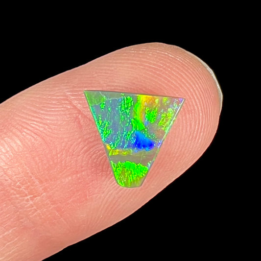 A loose, triangular shaped black opal from Lightning Ride, Australia.  The opal is predominantly green.