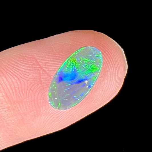 A loose, oval shaped black opal stone from Lightning Ridge, Australia.  The opal plays bright green and blue colors.