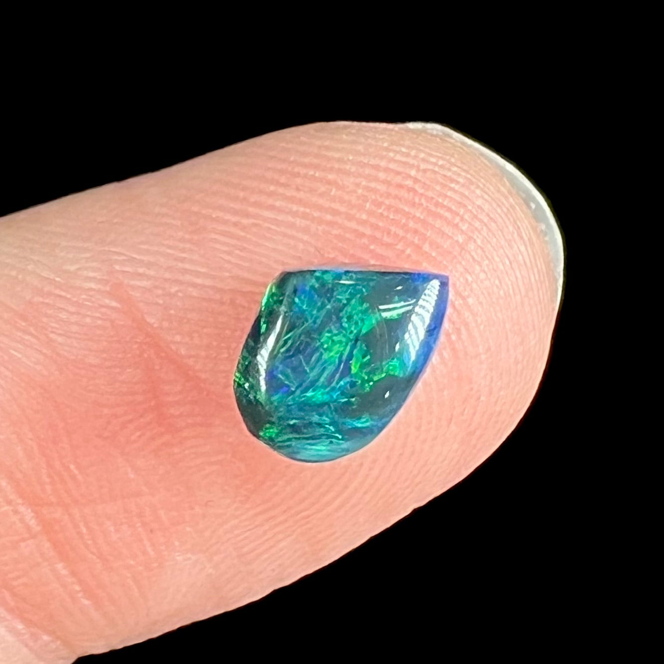 A freeform shaped natural black opal stone from Lightning Ridge, Australia.