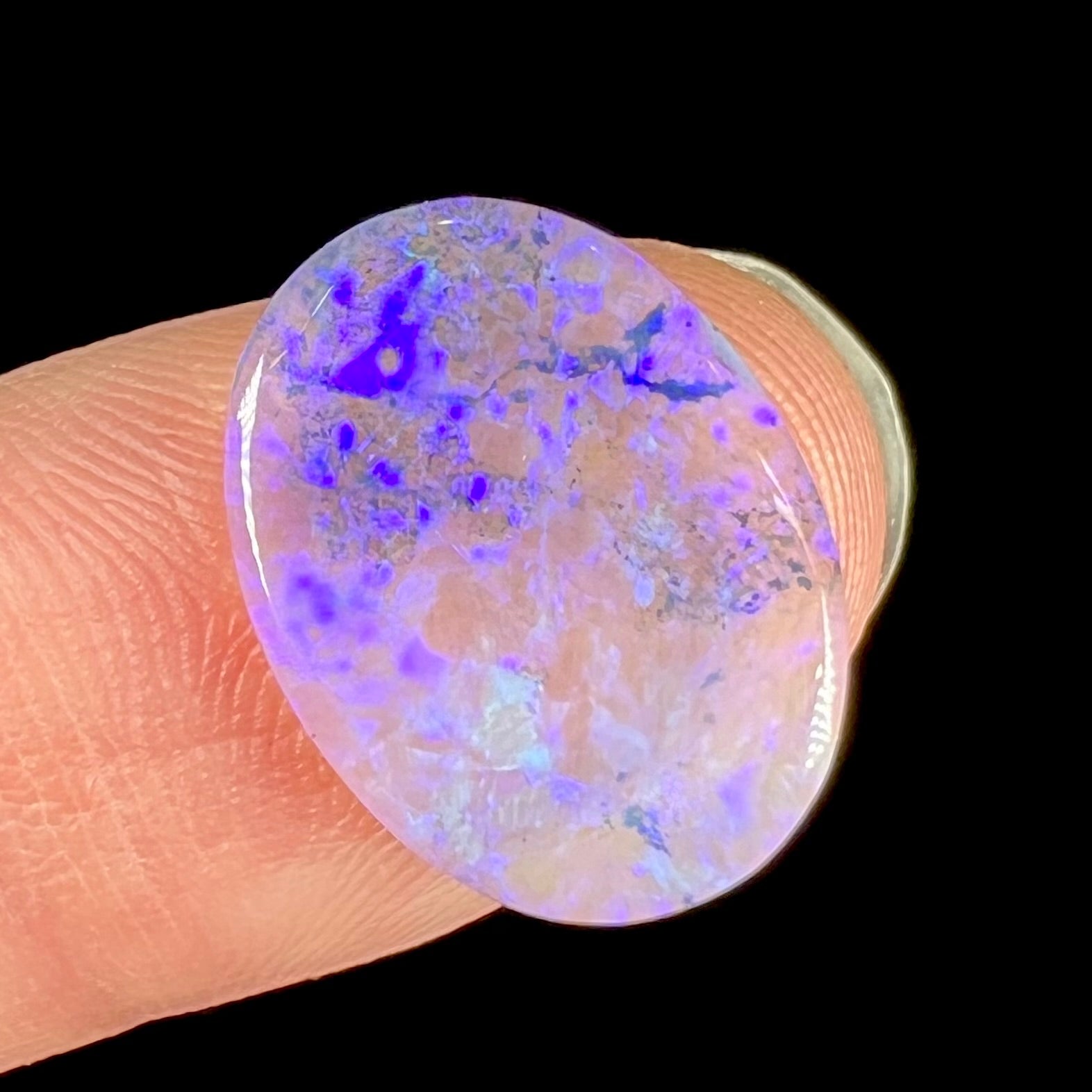 A loose, oval cabochon cut crystal opal from Lightning Ridge, Austalia that weighs 5.16 carats.  The stone has blue and purple colors.