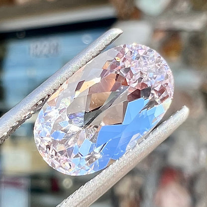 A loose, faceted oval cut kunzite gemstone.  The stone is a light pink color.