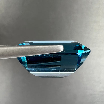 A loose, emerald cut London blue topaz gemstone.  The stone is a deep, dark blue color.