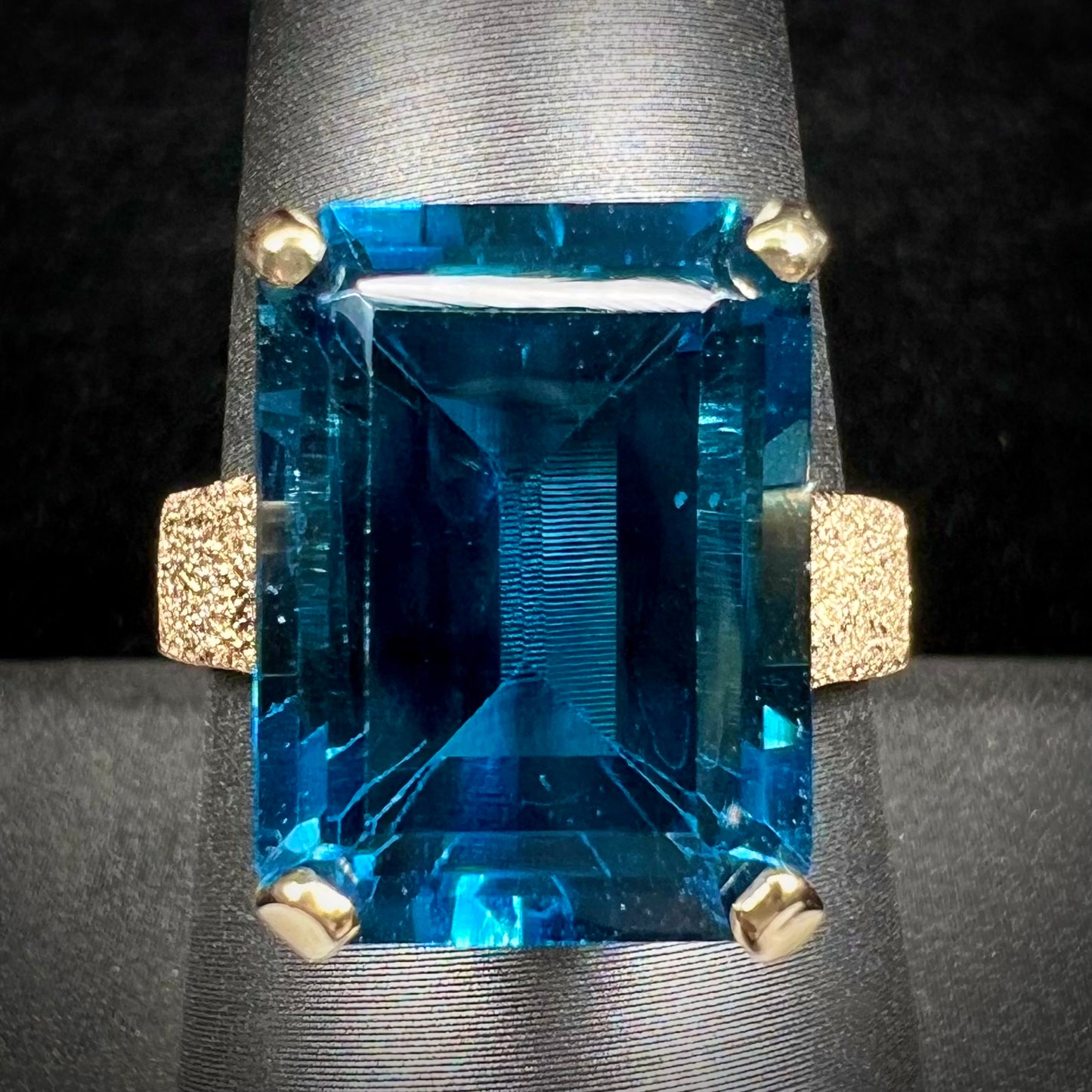 A ladies' yellow gold London blue topaz solitaire ring.  The ring is textured, and the topaz is emerald cut.