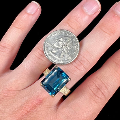 A ladies' yellow gold London blue topaz solitaire ring.  The ring is textured, and the topaz is emerald cut.