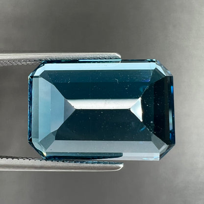 A loose, emerald cut London blue topaz gemstone.  The stone is a deep, dark blue color.