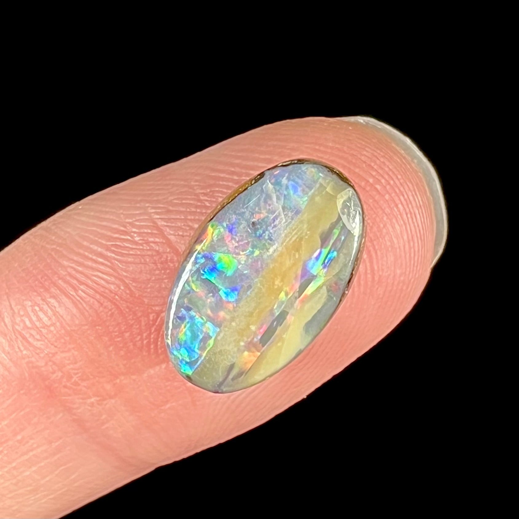 An oval cabochon cut boulder opal from Quilpie, Australia.  The opal has multicolor color play.