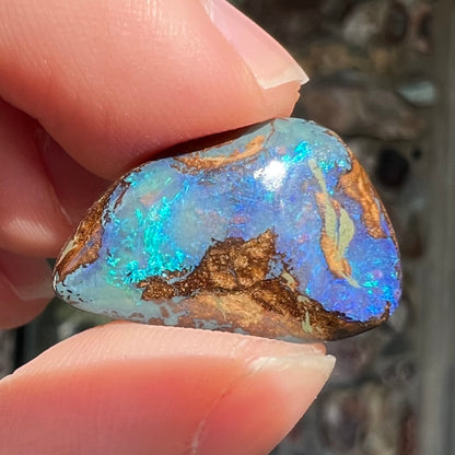 A freeform pear shaped boulder opal stone with blue color.