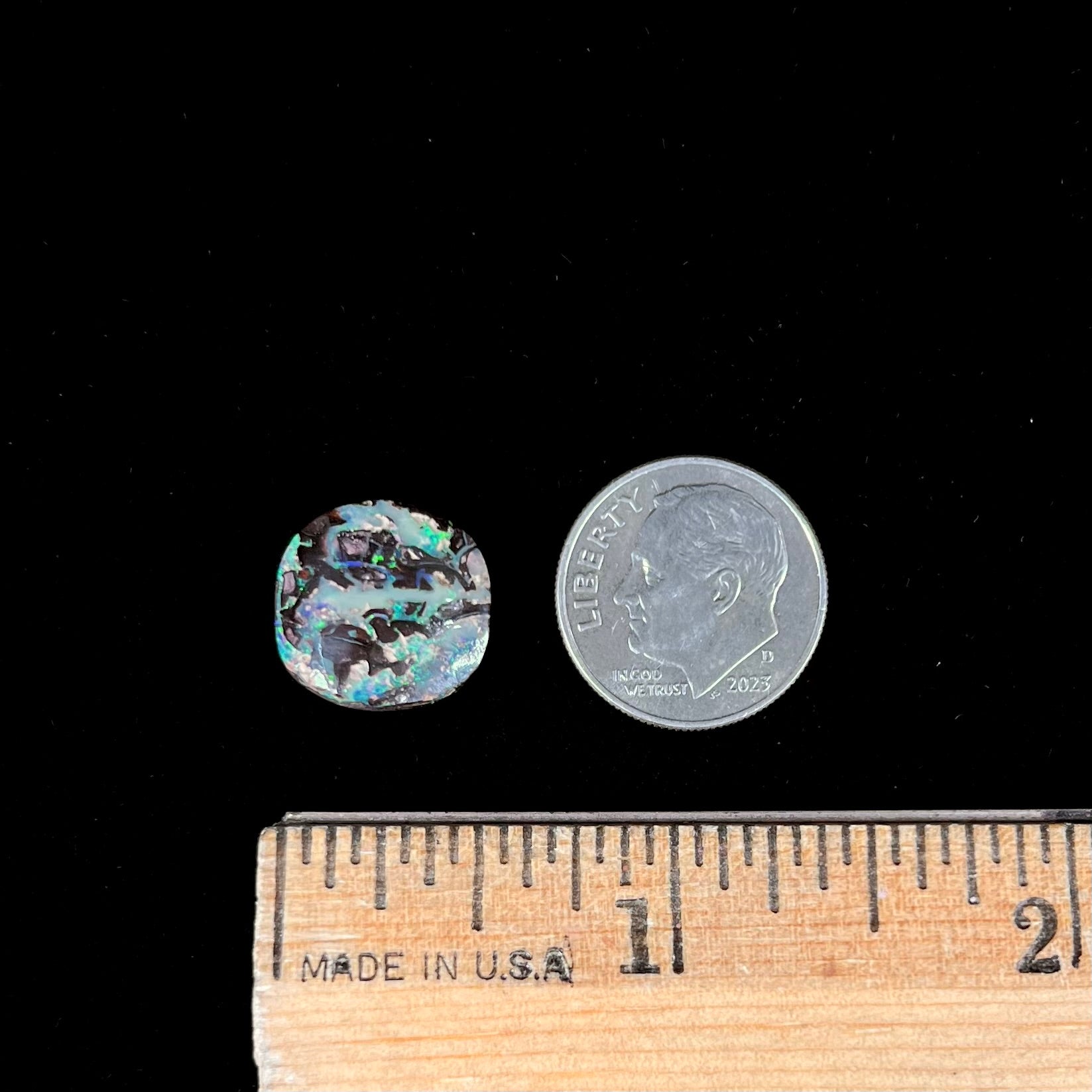 An off-round cabochon cut boulder opal stone from Koroit, Australia.  The opal has green, blue, and red colors.