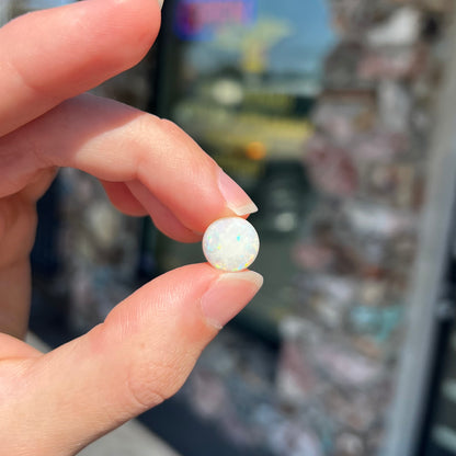 A loose, round cabochon cut white opal from Coober Pedy, Australia.  The opal has green fire.