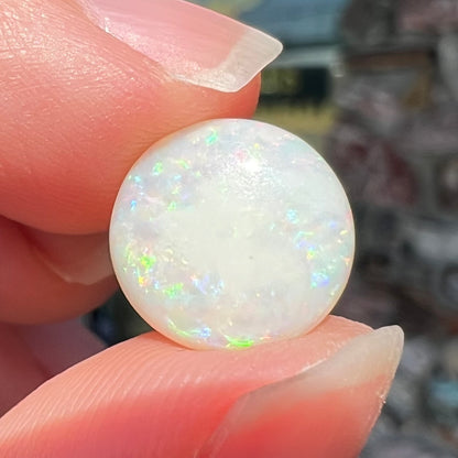 A loose, round cabochon cut white opal from Coober Pedy, Australia.  The opal has green fire.