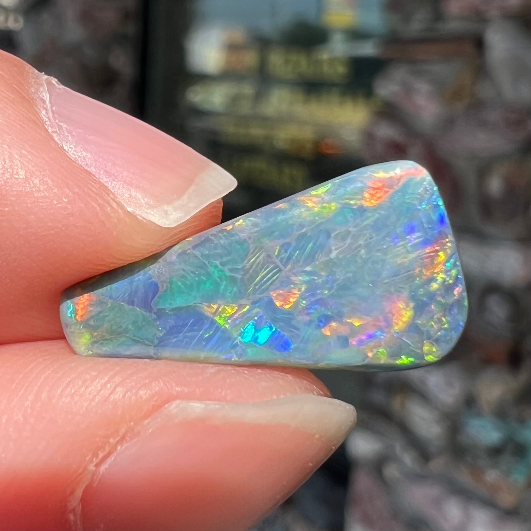 A loose, freeform triangle shaped black opal stone from Lightning Ridge, Australia that weighs 2.71 carats.