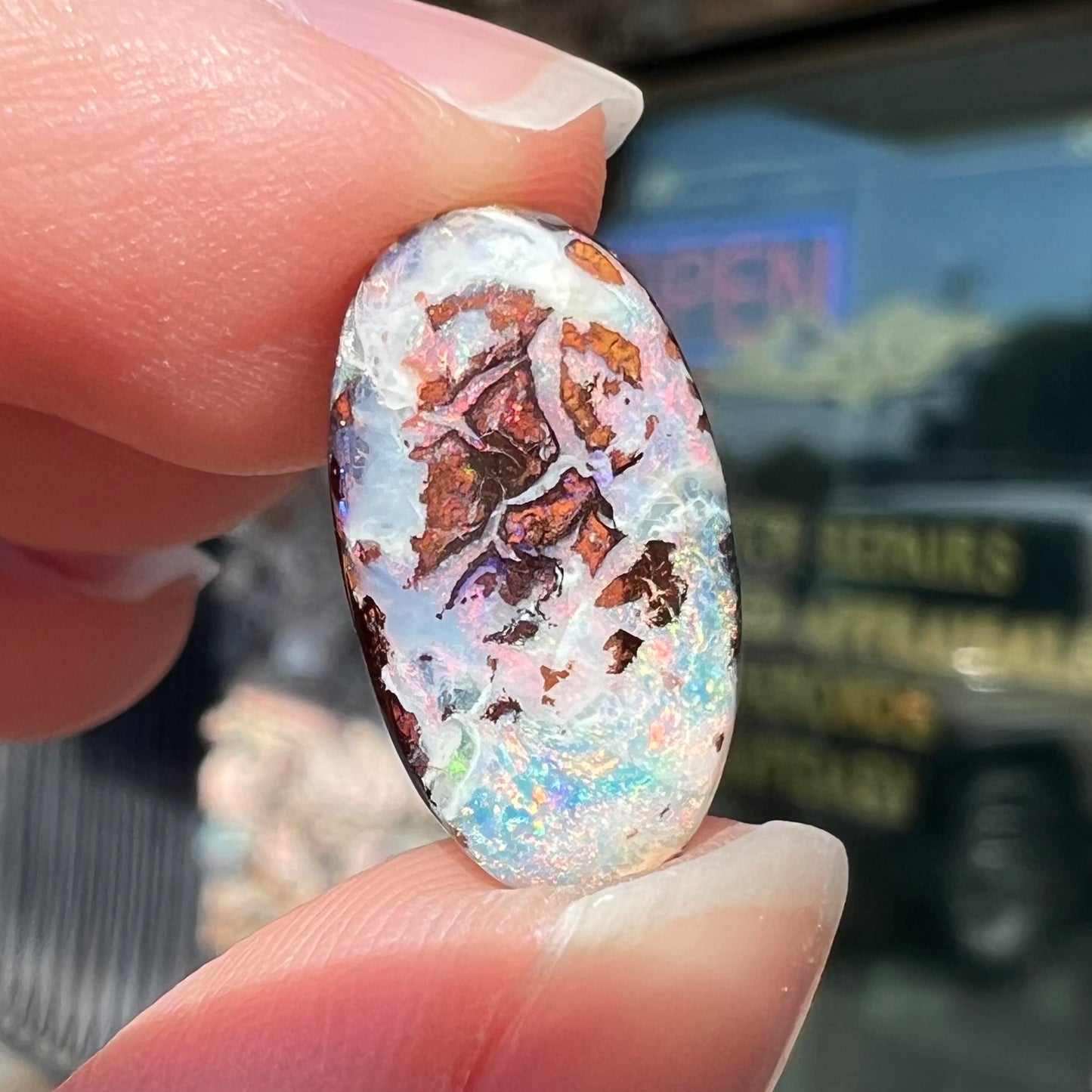 An oval cabochon cut boulder opal stone from Koroit, Australia.  The opal has a white body tone.