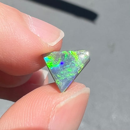 A loose, triangular shaped black opal from Lightning Ride, Australia.  The opal is predominantly green.