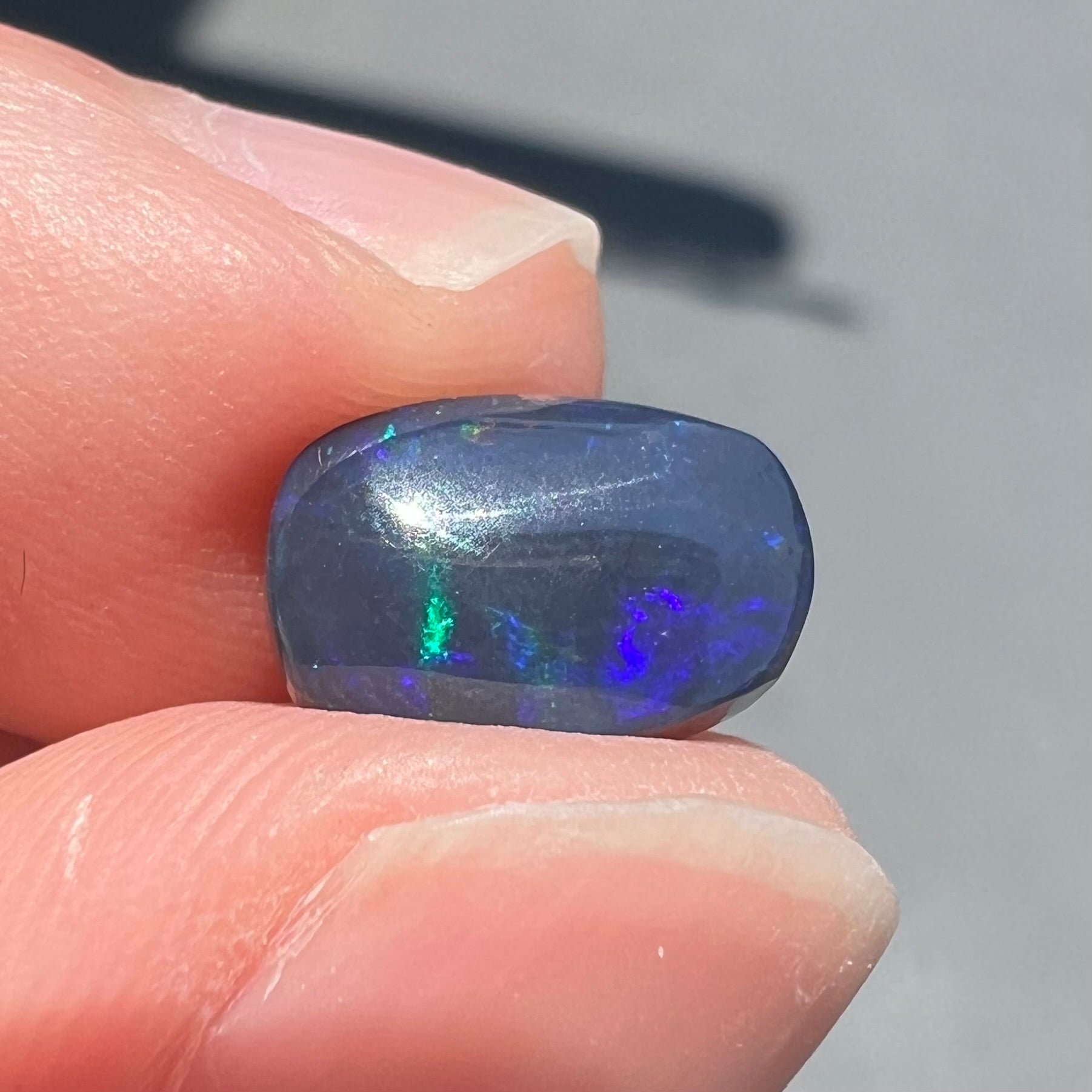 A loose Lightning Ridge black opal stone that shines colors of green, blue, and purple.