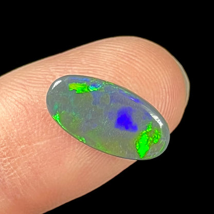 A loose, oval cut black opal stone from Lightning Ridge, Australia.  The opal plays with green and blue fire.