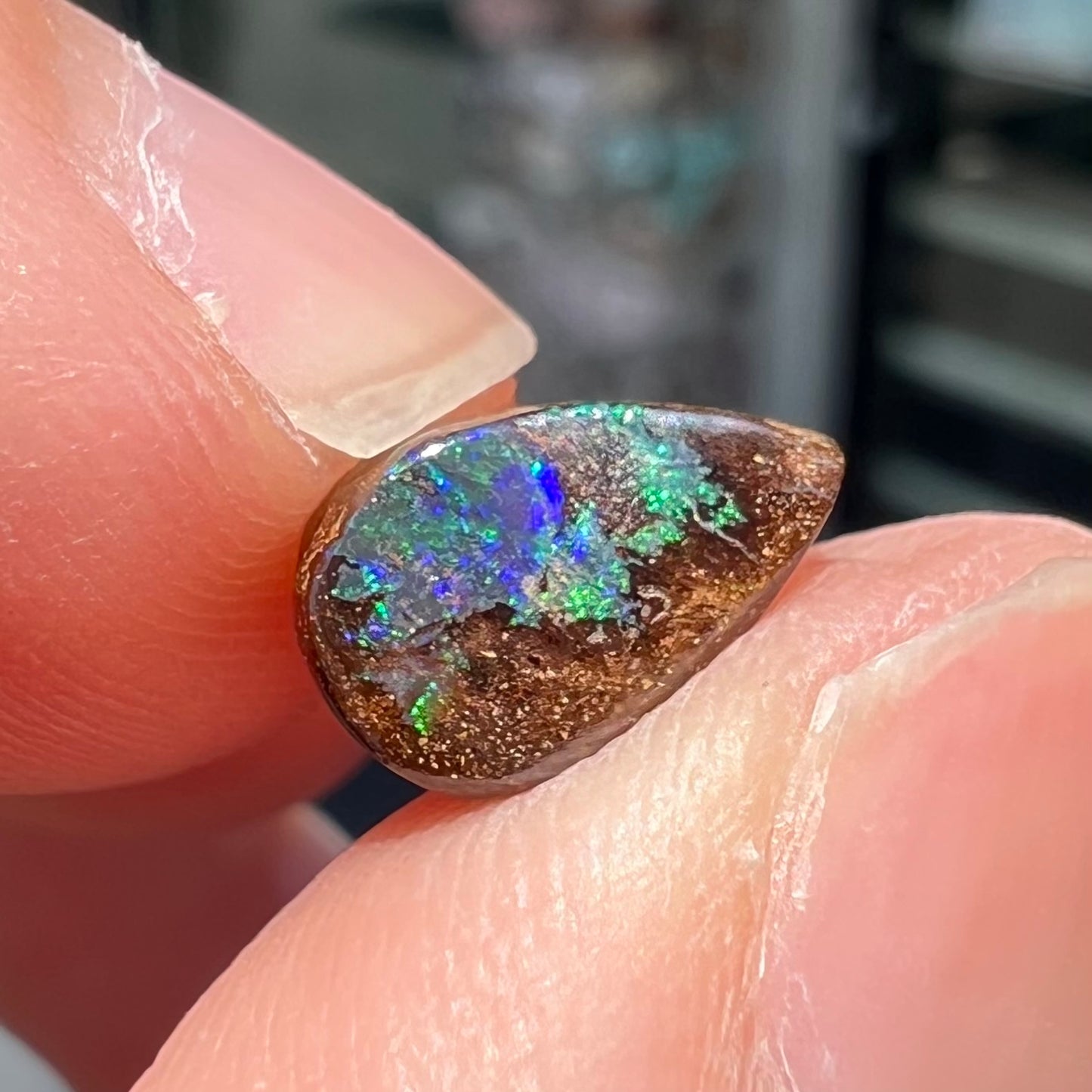 A loose, pear shaped boulder opal stone that flashes colors of green and blue.