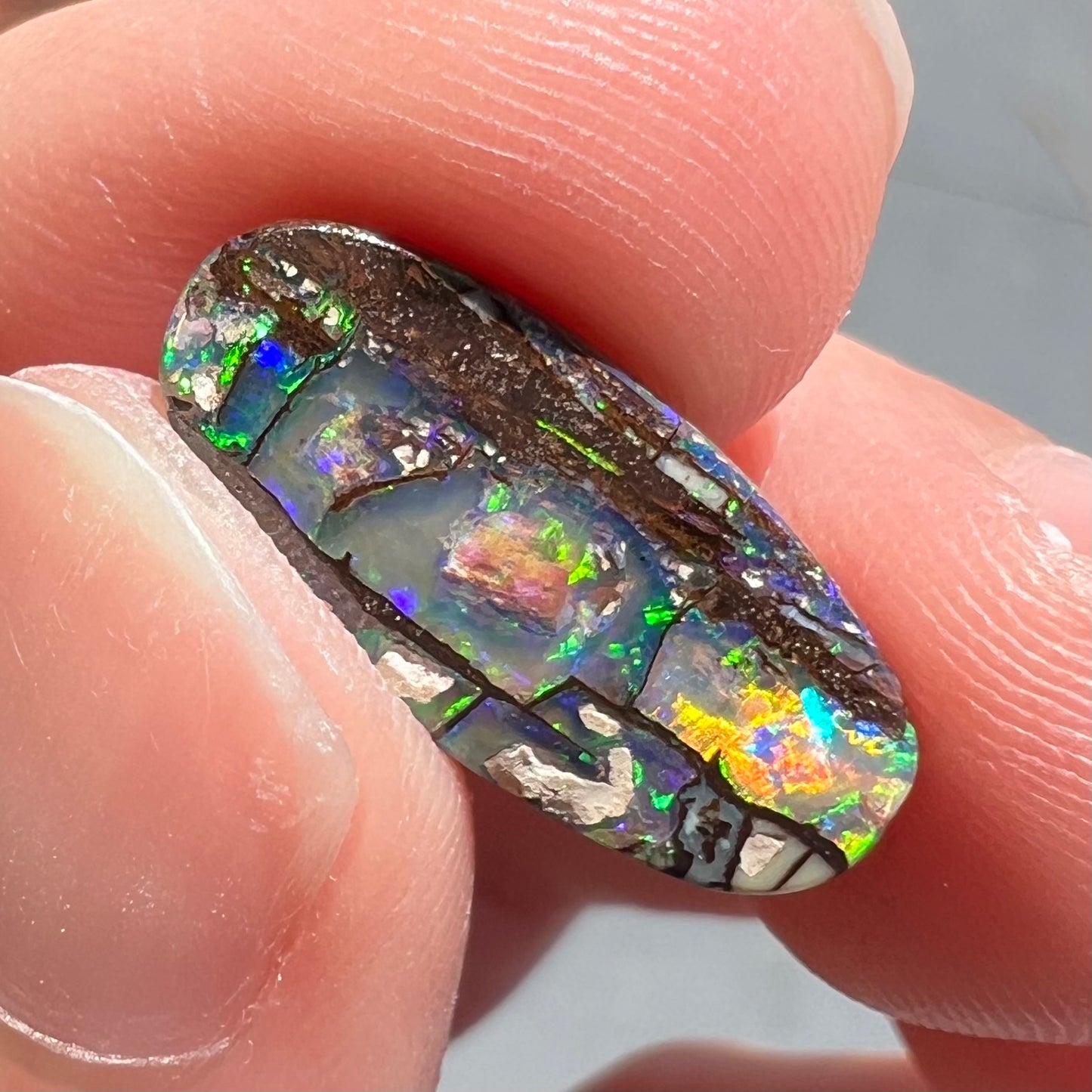 A loose, oval cut boulder opal stone from Koroit, Australia.  The opal shines green and blue colors.